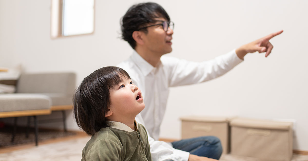 A man points out something to a toddler on the TV