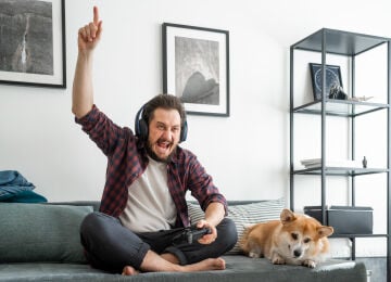 Un hombre en un sofá con su perro juega videojuegos